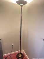 Full view of 72-inch black metal torchiere floor lamp plugged in and lit