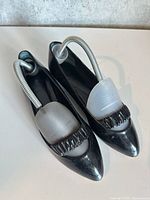 Top view of both black patent leather pumps with vamp detailing and shoe shapers inserted