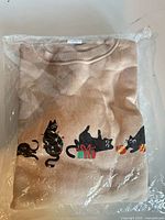 Front view of folded tan sweater with cat holiday graphic inside original plastic