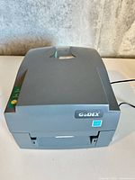 Front angled view of closed grey GoDEX label printer showing brand badge and LED panel