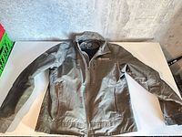 Front view of Kuhl olive jacket laid flat showing pockets and sleeves