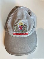Front view of grey baseball cap showing coat of arms embroidery and Luxembourg text