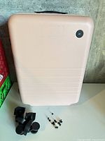 Front view of pink suitcase with Monos badge, wheels and screws shown separately
