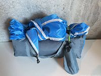 Rolled blue and gray tent with straps on light surface
