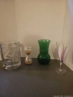 All four items lined up: clear Circus Circus mug, hourglass, green vase, painted wine glass