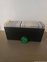 Black card box filled with Pokemon cards and green coin in front