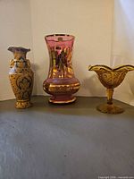 Group view of brass vase, cranberry glass vase and amber candy dish
