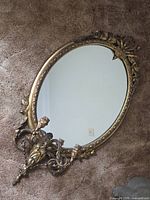 Full view of oval gilt mirror with attached three-arm candle sconce