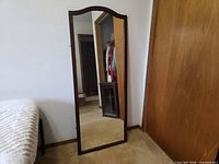 Tall arched-top mirror leaning against wall beside bed