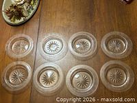 Eight clear crystal plates laid out showing Greek Key rim and starburst centers