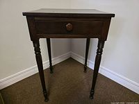 Front view of dark brown solid wood side table showing drawer with wooden knob and turned legs