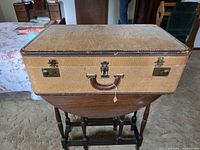 Full view of closed tan suitcase showing leather handle, brass latches, and overall wear