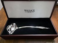Ladle resting inside open velvet-lined wooden presentation box showing Wallace Silversmiths logo