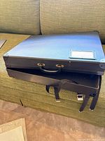 Closed black portfolio case showing handle, strap, buckle and corner protectors