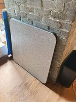 Square folding card table leaning against wall, showing top surface