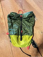 Front view showing green ripstop body, yellow lower panel, roll-top closure, red buckle