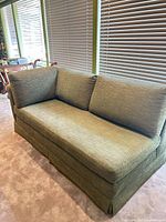 Full view of olive green sofa showing cushions, arm, and skirt