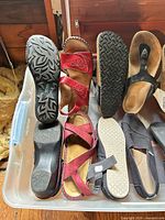 Various sandals and clogs in storage bin showing soles and uppers