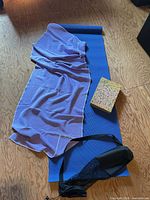 Blue yoga mat with lavender towel, one foam block and mesh bag visible