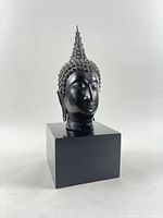 Front view of dark patina bronze Thai Buddha head on black stand