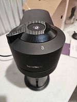Top and side view of Vertuo Next machine showing lid, lock symbol, Nespresso logo, cup stand