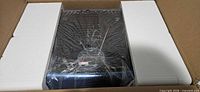 Vibration plate inside carton with foam inserts, protective plastic wrap over blue unit