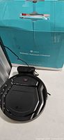 Robotic vacuum on table connected to charging dock in front of original box