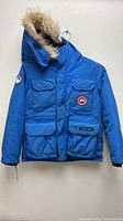 Full front view of blue Canada Goose jacket on hanger, hood with fur trim visible