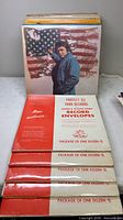 Stack of LPs with Johnny Cash “Ragged Old Flag” front, six sealed packs of inner sleeves in foreground