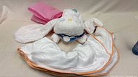 Plush bunny spread over white peach-trim blanket with pink bag visible