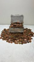 Ornate pewter-finish trinket box overflowing with copper pennies, coins spread around base