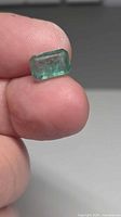 Emerald held between fingers showing overall size and color