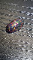 Top view of oval black opal showing multicoloured pinfire pattern