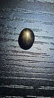 Loose oval black star sapphire on textured surface, showing cabochon profile and star effect