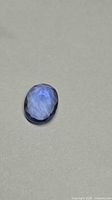 Oval faceted fluorite resting on neutral surface showing blue hue