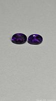 Two oval deep-purple amethysts on neutral background