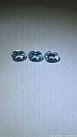 Three light blue oval-cut gemstones displayed on neutral background