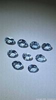 Nine oval faceted light blue aquamarine stones on neutral background