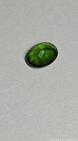 Top view of deep green oval chrome diopside on gray surface