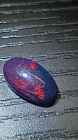 Oval black opal cabochon showing red flash on dark surface