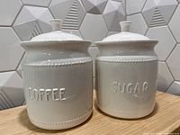 Front view of both white ceramic canisters showing raised COFFEE and SUGAR text