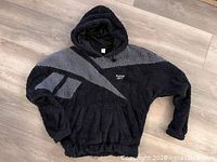 Front view of black and grey Reebok teddy pullover hoodie with logo and pockets visible