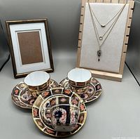 Tea cups, saucers, picture frame and necklaces displayed together