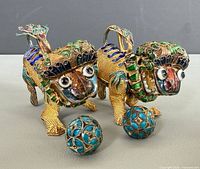 Front three-quarter view of both enamel foo dogs each holding a cloisonné sphere