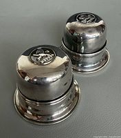 Two silver-plated cylindrical ring boxes side by side showing overall form and crest on one lid