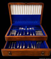 Open two-tier wooden chest showing arranged silver-plated flatware pieces in blue felt slots