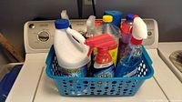 Overall lot showing blue basket with assorted cleaning bottles on washer