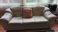 Front view of beige leather 3-seat sofa with throw pillow