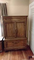 Front view of armoire closed showing exterior doors, drawer and footed base