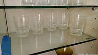 Five etched glass tumblers on glass shelf